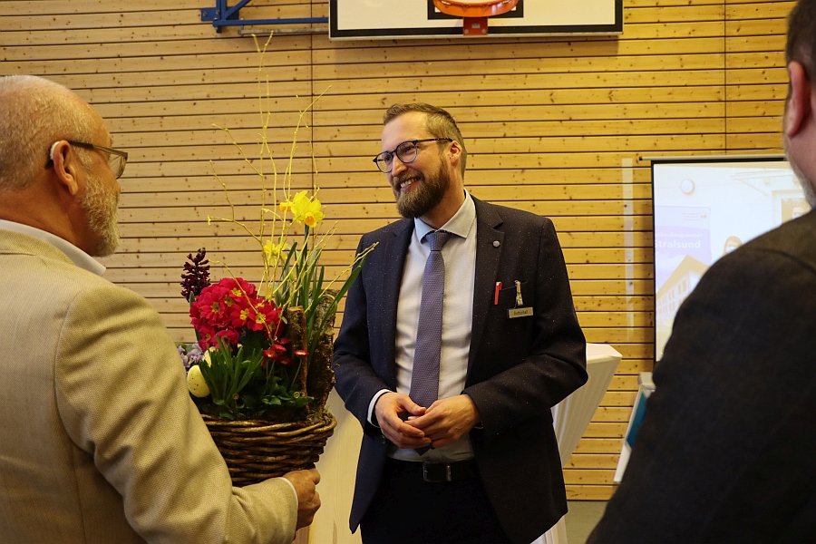 Das Bild zeigt die Übergabe einer Blumenschale mit Frühlingsblumen an den Anstaltsleiter. 